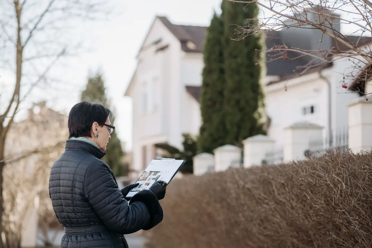 Property professional reviewing a floor plan on a clipboard outside a house